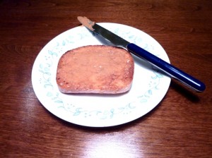A slice of peanut butter on a plate with a knife